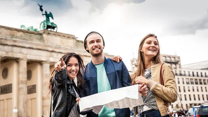 Drei Freunde stehen vor dem Brandenburger Tor und haben eine Karte in der Hand.