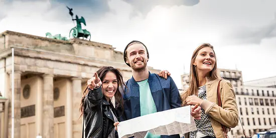 Drei Freunde stehen vor dem Brandenburger Tor und haben eine Karte in der Hand.