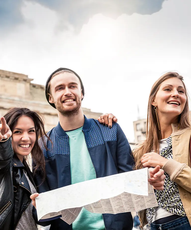 Drei Freunde stehen vor dem Brandenburger Tor und haben eine Karte in der Hand.