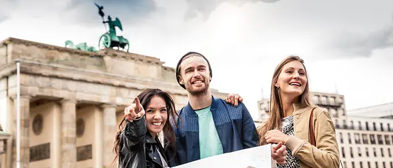 Drei Freunde in Berlin - Reiserücktrittsversicherung Deutschland Drei Freunde stehen vor dem Brandenburger Tor und haben eine Karte in der Hand.