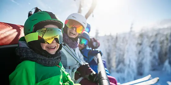 Eine Familie sitzt im Skilift. Im Hintergrund sind verschneite Bäume zu sehen. 