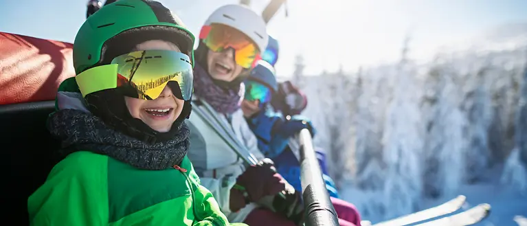 Eine Familie sitzt im Skilift. Im Hintergrund sind verschneite Bäume zu sehen. 