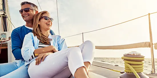 Ein Ehepaar sitzt auf einem Segelschiff. Der Mann hält seine Frau in den Armen.