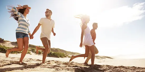 Vier Freunde laufen am Strand in Richtung Wasser