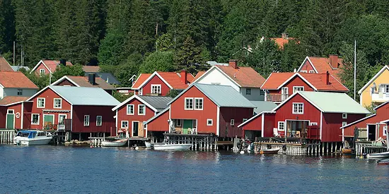 Kleine rote Häuser stehen am Wasser. Im Hintergrund ist ein Wald. 