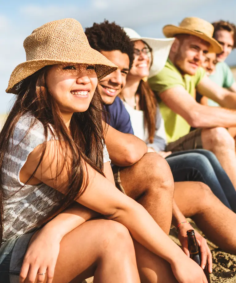 Sechs Freunde sitzen am Strand und genießen die Sonne.