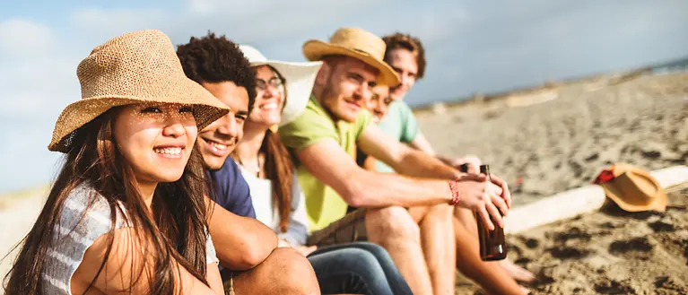 Sechs Freunde sitzen am Strand und genießen die Sonne.