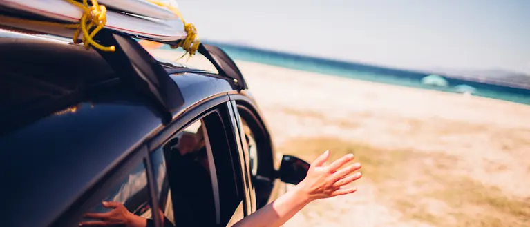 Ein Auto steht am Strand. Eine Person streckt ihren Arm aus dem Fenster. 