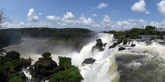 Man erkennt einen großen Wasserfall. Im Hintergrund sind viele Bäume und blauer Himmel zu sehen.