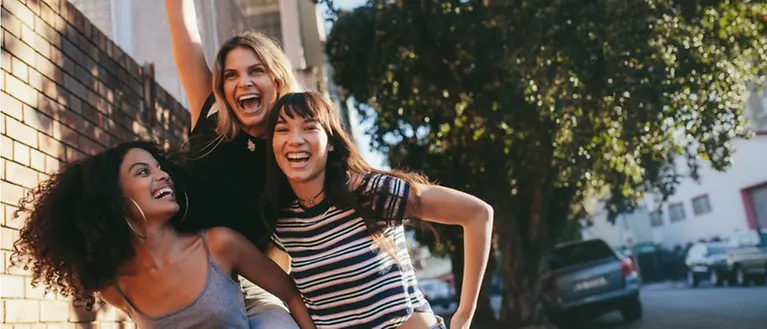 Drei junge Frauen stehen auf einem Fußweg und lachen.