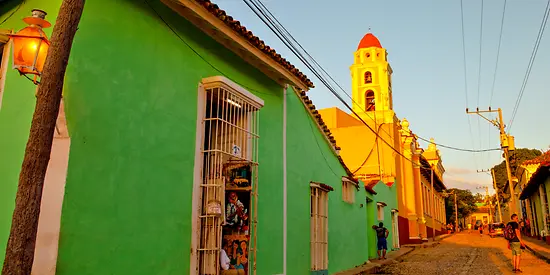 Ein Straße in Kuba. Auf der linken Seite ist ein grünes Gebäude und eine Kirche. 