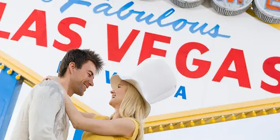 Ein Mann und eine Frau stehen vor einem großen Las Vegas Schild und lächeln sich an. 