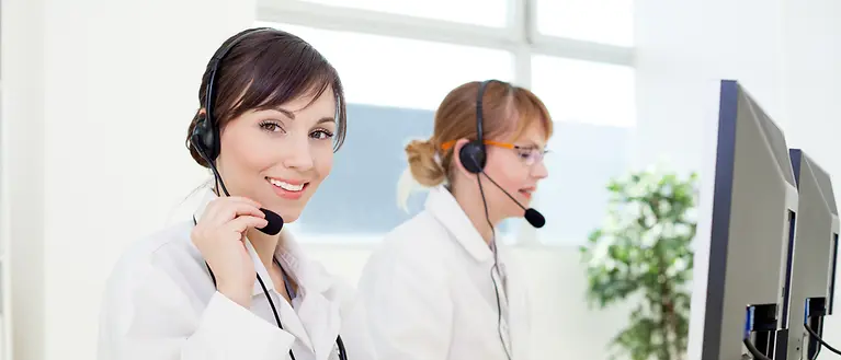 Zwei Frauen mit einem Headset sitzen am Computer und arbeiten. 