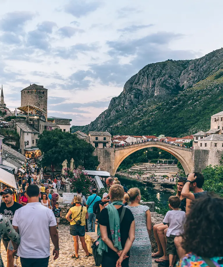 Man sieht mehrere Personen, die auf einem kleinen Weg entlang der Stadt längst laufen. Im Hintergrund ist eine Brücke zu sehen.