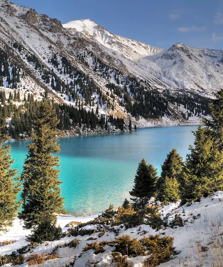 Man sieht einen hellblaue See, der inmitten von Bergen liegt. Diese Berge sind mit Schnee bedeckt.