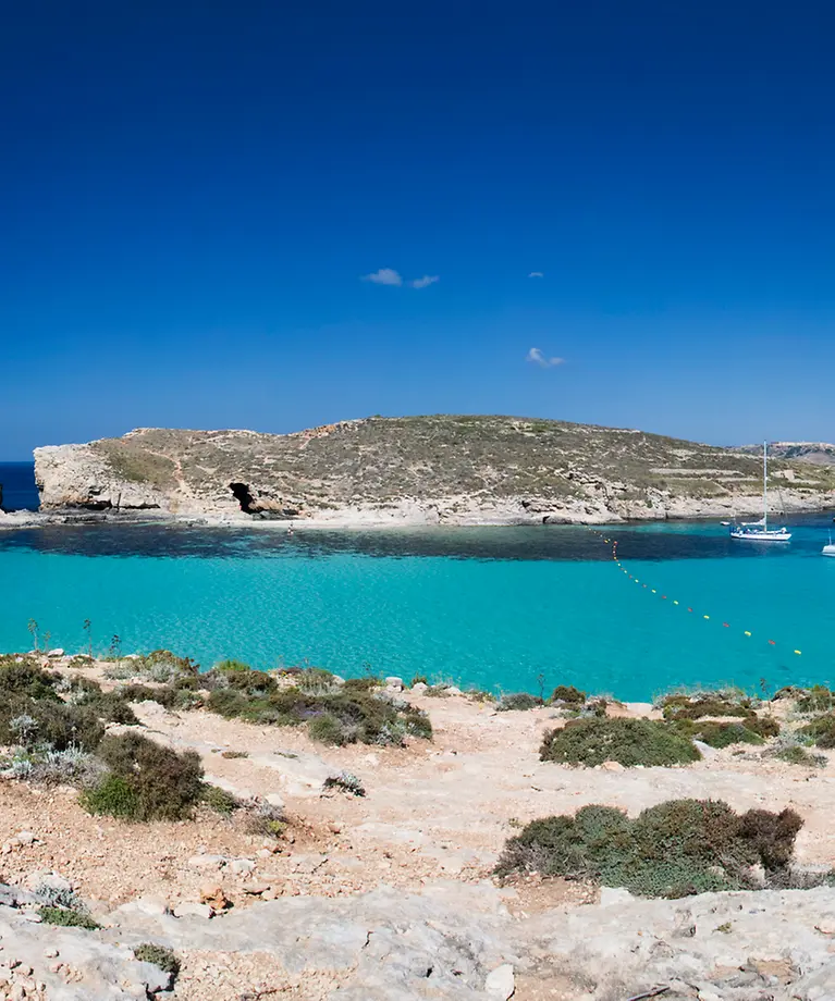 Man erkennt eine Bucht mit türkisem Wasser. Im Hintergrund ist eine kleine Insel zu sehen. 