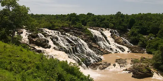 Man sieht einen großen Wasserfall, der umgeben ist von grünen Bäumen.