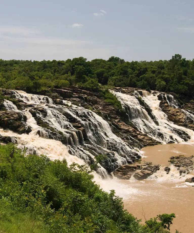 Man sieht einen großen Wasserfall, der umgeben ist von grünen Bäumen.