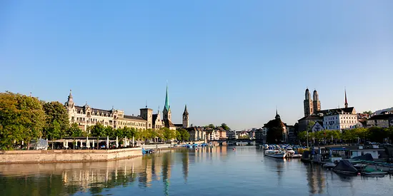 Man sieht eine Stadt durch die ein Fluss hindurch fließt. Im Hintergrund sieht man eine kleine Brücke.