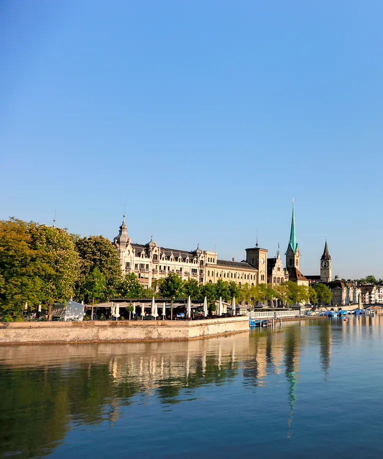 Man sieht eine Stadt durch die ein Fluss hindurch fließt. Im Hintergrund sieht man eine kleine Brücke.