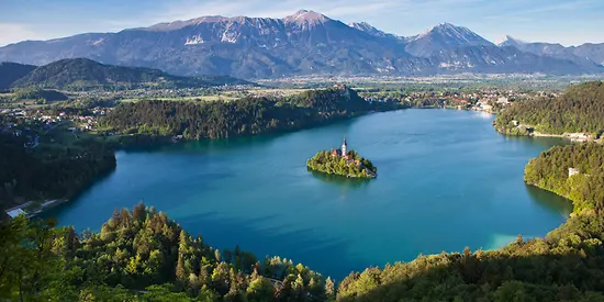 Man sieht einen großen See. In der Mitte des Sees befindet sich eine kleine Insel. Im Hintergrund sieht man eine Berglandschaft.