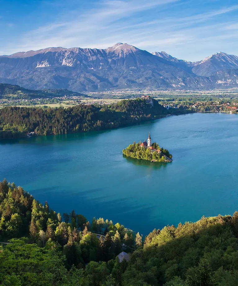 Man sieht einen großen See. In der Mitte des Sees befindet sich eine kleine Insel. Im Hintergrund sieht man eine Berglandschaft.