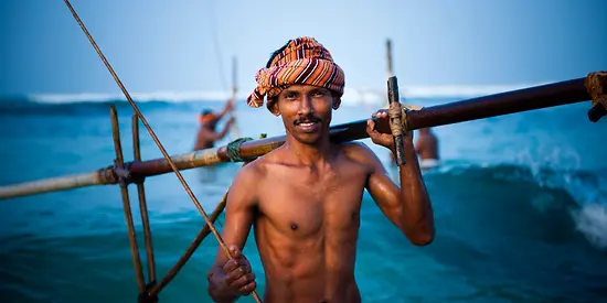 Man sieht einen Stelzenfischer, der im Meer steht und sein Equipment in der Hand hält.