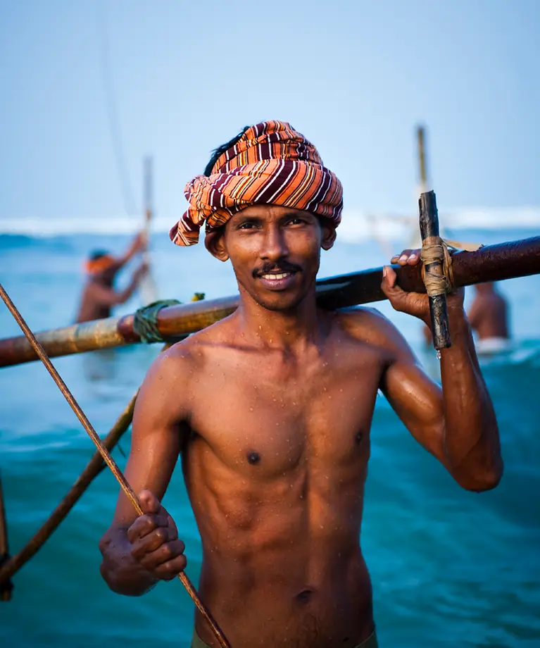 Man sieht einen Stelzenfischer, der im Meer steht und sein Equipment in der Hand hält.