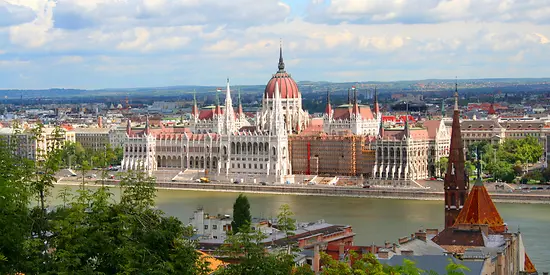 Man sieht einen Fluss. Rechts im Bild ist eine Stadt zu sehen. Im Hintergrund sind Berge zu sehen. 