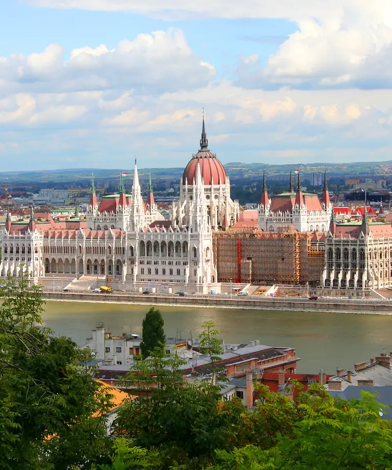 Man sieht einen Fluss. Rechts im Bild ist eine Stadt zu sehen. Im Hintergrund sind Berge zu sehen. 