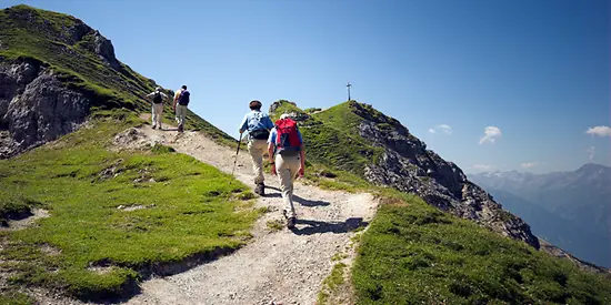 Man sieht mehrere Wanderer, die entlang eines Wanderwegs einen Berg erklimmen, um zur Spitze zu gelangen.