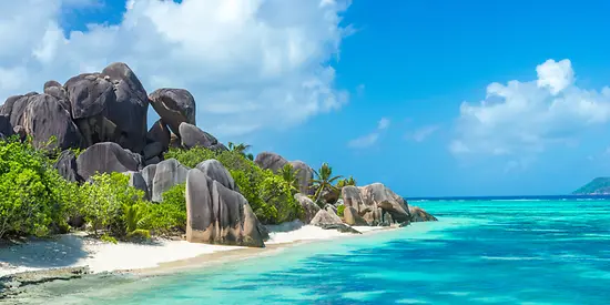 Man sieht einen Sandstrand mit Granitfelsen.