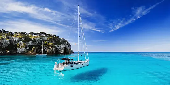 Ein kleines Segelschiff ankert in einer Bucht mit türkisfarbendes Wasser.