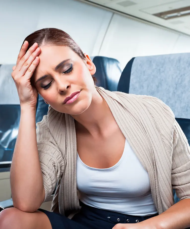 'Eine Frau sitzt im Flugzeug und hält mit ihrer Hand ihren Kopf. 