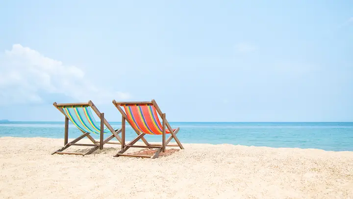 Zwei Liegestühle stehen am Strand. Im Hintergrund ist das Wasser.