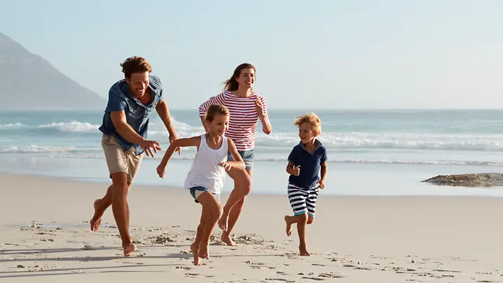 Eine Familie läuft am Strand. Im Hintergrund kann man das Wasser und einen Berg sehen.