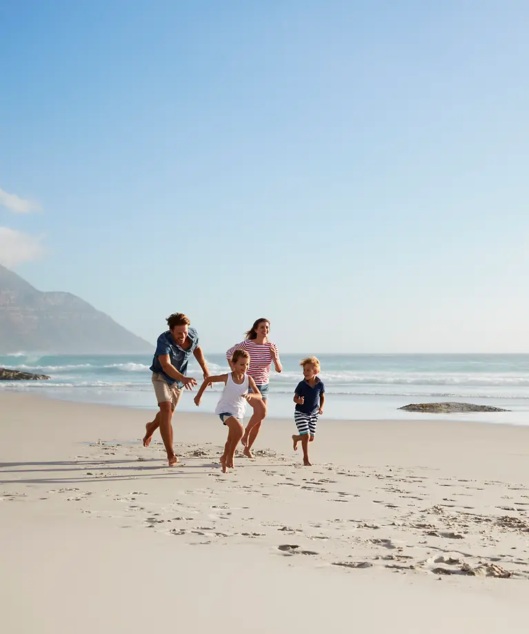 Eine Familie läuft am Strand. Im Hintergrund kann man das Wasser und einen Berg sehen.