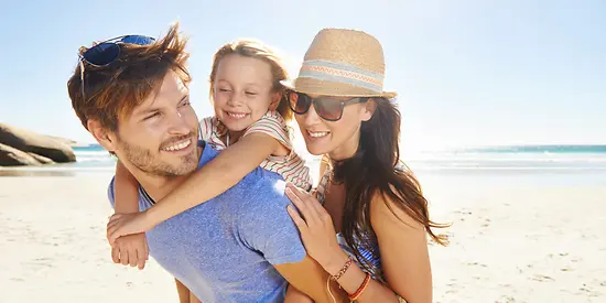 Mutter, Vater und deren Tochter sind am Strand. Im Hintergrund ist das Meer. 