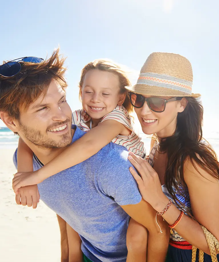 Mutter, Vater und deren Tochter sind am Strand. Im Hintergrund ist das Meer. 