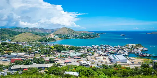 Man erkennt eine kleine Stadt in Papua-Neuguinea von oben. Im Hintergrund sieht man Wasser.