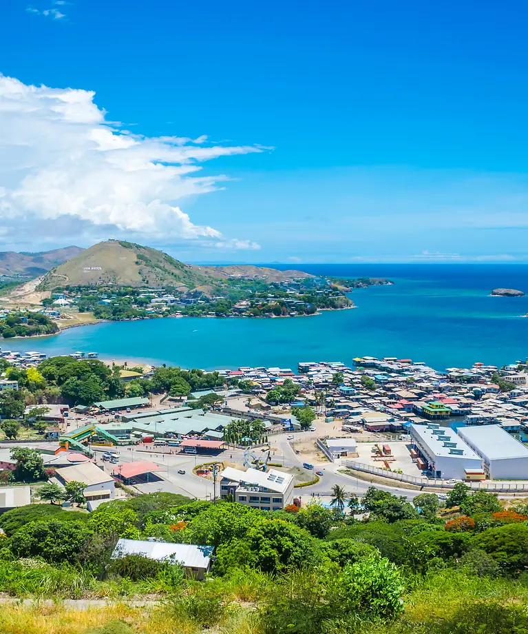 Man erkennt eine kleine Stadt in Papua-Neuguinea von oben. Im Hintergrund sieht man Wasser.