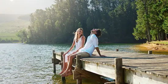 Ein Mann und eine Frau sitzen auf einem Steg, der ins Wasser hineinführt und lachen.