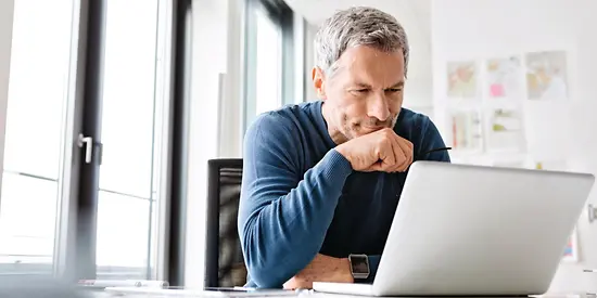 Ein Mann schaut nachdenklich auf seinen Laptop, der vor ihm steht.