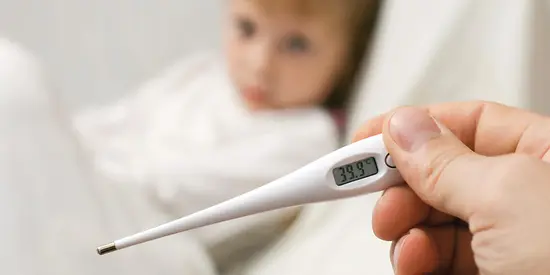 Im Vordergrund erkennt man ein weißes Fieberthermometer. Im Hintergrund ist verschwommen ein kleines Kind zu erkennen. 