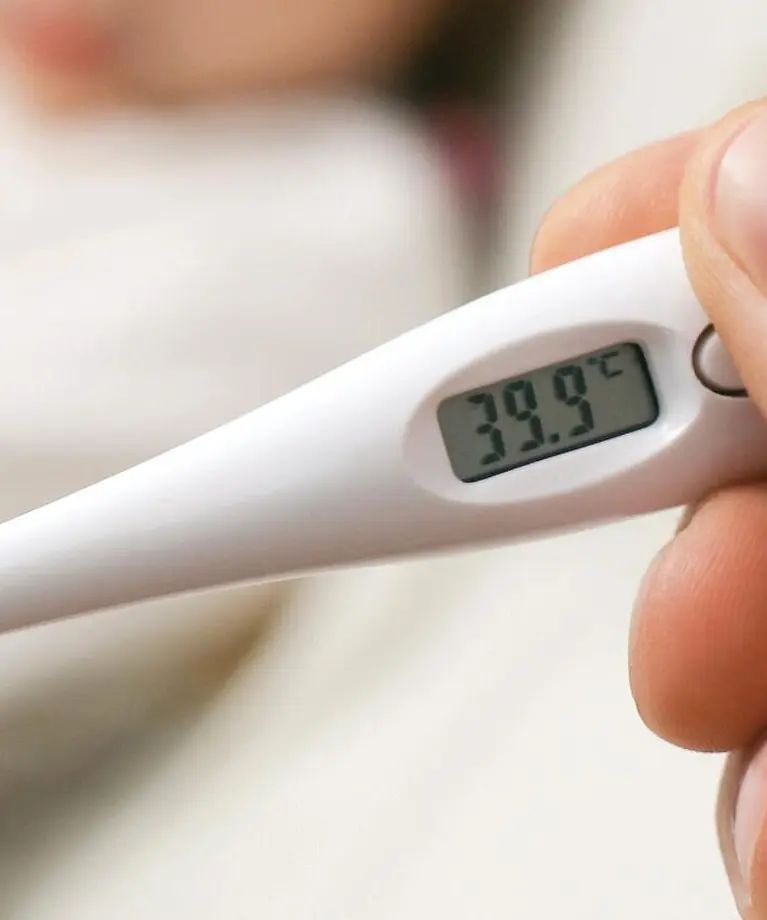 Im Vordergrund erkennt man ein weißes Fieberthermometer. Im Hintergrund ist verschwommen ein kleines Kind zu erkennen. 