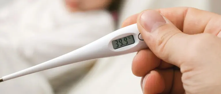 Im Vordergrund erkennt man ein weißes Fieberthermometer. Im Hintergrund ist verschwommen ein kleines Kind zu erkennen. 