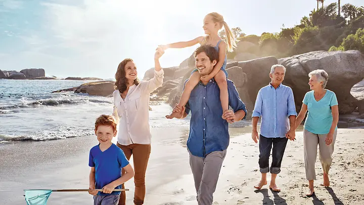 Mutter, Vater und deren Tochter gehen gemeinsam mit Oma und Opa am Strand spazieren.