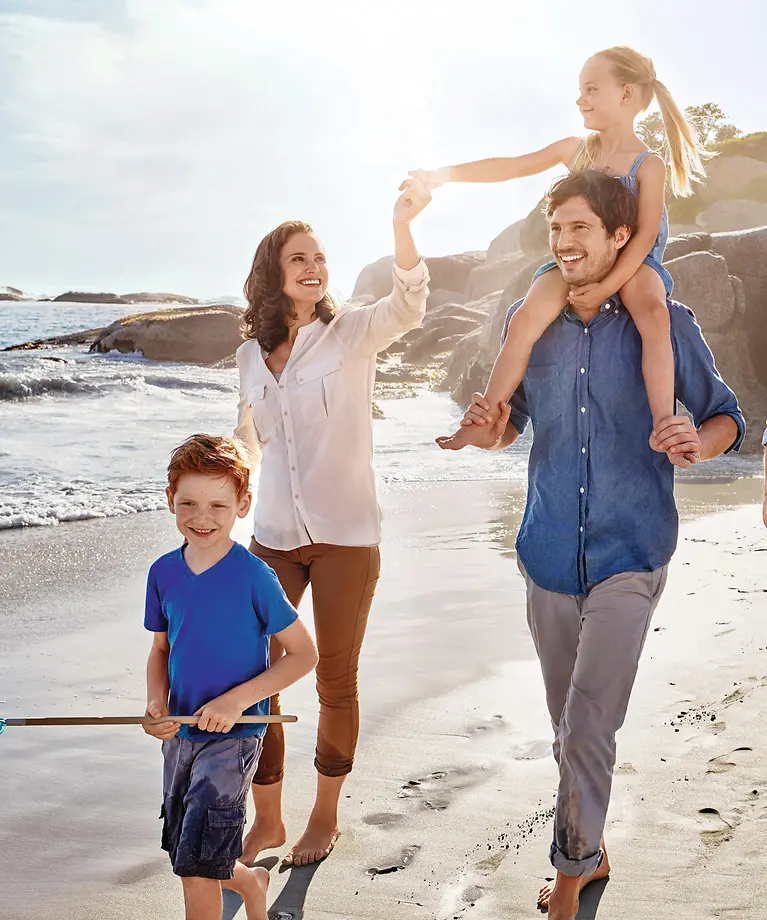 Mutter, Vater und deren Tochter gehen gemeinsam mit Oma und Opa am Strand spazieren.