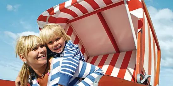 Eine Mutter und ihr Kind sitzen in einem Strandkorb. Beide lachen. 