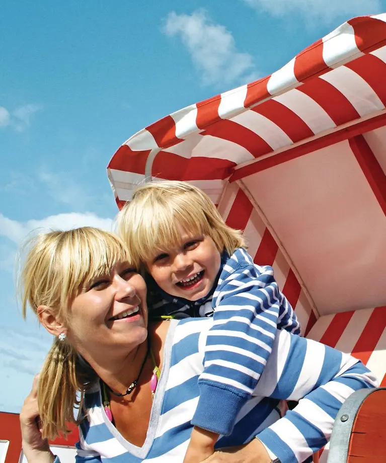 Eine Mutter und ihr Kind sitzen in einem Strandkorb. Beide lachen. 